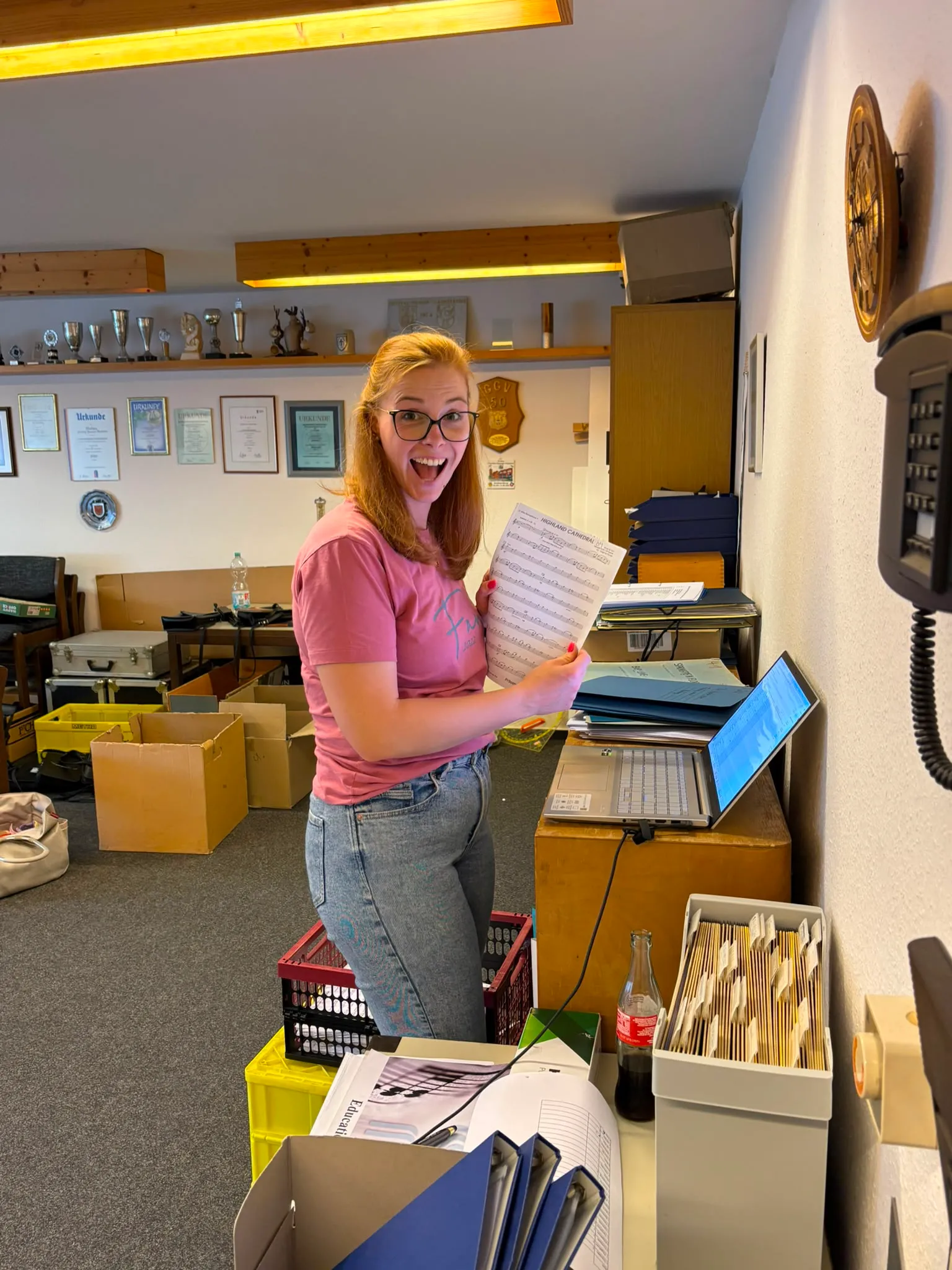 Musikerin im Probenraum mit Notenblatt, im Hintergrund Pokale und Urkunden